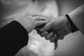 Grayscale closeup of the groom touching the priest's cross