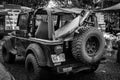 Grayscale of a Jeep with a surfboard in the truck with outdoor retailers in the background