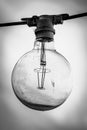 Grayscale of a light bulb hanging from a thin silver power line cable against the background of sky