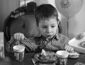 Grayscale of a little boy eating cake sitting around the table Royalty Free Stock Photo