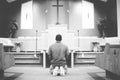 Grayscale of a male on his knees praying in the church with a blurred background Royalty Free Stock Photo