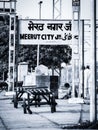 Grayscale of a Meerut City sign above hay wagons with a man sitting in the background