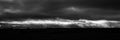 Grayscale panoramic shot of dark thunder sky over silhouettes of wind turbines