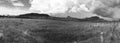 Grayscale panoramic shot of a field with a background of hills