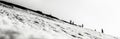 Grayscale panoramic shot of a snowy hillside pith lots of walking people silhouette