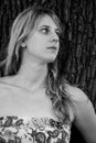 Grayscale photo of a blonde girl leaning against a tree Royalty Free Stock Photo