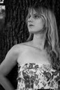 Grayscale photo of a blonde girl leaning against a tree Royalty Free Stock Photo