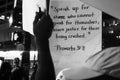 Grayscale of proverbs verse 31:8 handwritten on a sign raised high in a group of protesters