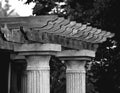Grayscale of Roman columns topped with a wooden pergola structure