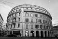 Grayscale of a round building in downtown Lausanne in Switzerland with passing cars and people