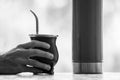 Grayscale selective focus shot of a hand holding a calabash mate cup with straw