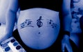 Grayscale selective focus shot of music notes on pregnant belly