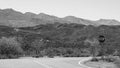 Grayscale shot of a country road with a stop sign, surrounded by hills. Royalty Free Stock Photo