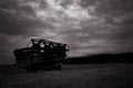 Grayscale shot of a large combine in the field with clouds above