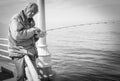 Grayscale shot of an old fisher man fishing from the sea in Santa Monica Pier