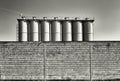 Grayscale shot of the outside of an industrial building with a stone wall and big tubes behind