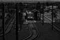 Grayscale shot of a passenger train curving around a bend in a large industrial railyard.