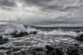 Grayscale shot of wavy sea hitting the rocky beach