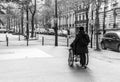 Grayscale shot of a woman pushing a person in a wheelchair on the streets of Paris, France.