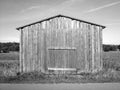 Grayscale shot of a wooden cabin in a field under a cloudy sky