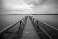 Grayscale shot of a wooden pier in the ocean with a single boat under the dark cloudy sky