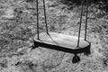 Grayscale shot of a wooden swing hanging from ropes