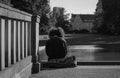 Grayscale shot of a young curly-haired person sitting on the edge of a bridge.