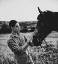 Grayscale shot of a young male petting a horse in a field under the sunlight