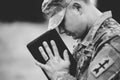 Grayscale shot of a young soldier praying while holding the bible