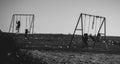Grayscale of swings outdoors and children silhouettes playing there, the Balkan lifestyle in towns