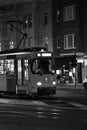 Grayscale of a tram going through town streets at night on the street