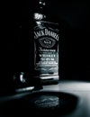 Grayscale vertical shot of a bottle of Jack Daniels whiskey with its reflection below it