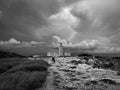 Grayscale view of a human walking toward the Faro Los Morrillos under the cloudy sky