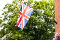 Great Britain flag on the house with flowers. State flaf with blue sky and clouds in the background.