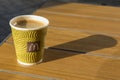 Great coffee in the original paper cup in McDonalds. It is located on a wooden surface. Close-up