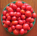 Wonderful red of different sizes and shapes of delicious tomatoes lie piled in a large round green tray on a brown wooden table. Royalty Free Stock Photo