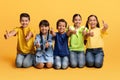 Happy diverse multietnic children showing thumb up, sitting on floor