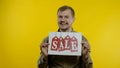 Great discounts. Happy cheerful blonde man in blue shirt showing Sale word advertisement inscription