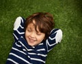 Great giggles. Little boy lying on the grass with his hands behind his head.