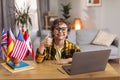 Great international education. Postive little boy showing thumb up gesture, desk with laptop and various foreign flags