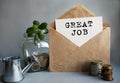 GREAT JOB text is written on white paper on an antique envelope, which lies on the table along with a stack of coins, a glass jar Royalty Free Stock Photo