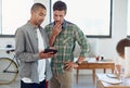 Great minds at work. two male coworkers looking at a digital tablet in an office.