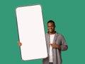 Great mobile offer. Happy black man pointing at huge empty smartphone in his hand, showing mockup for your design Royalty Free Stock Photo