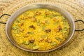 Great and popular Valencian rice paella presented in a paella pan with green flat beans, chunks of stewed chicken, white garrafon