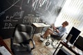 Great results. Happy young male trader in a wheelchair holding some documents and looking at charts and graphs on Royalty Free Stock Photo