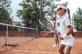 Great teamwork on court! Side view of sporty beautiful woman and girl playing tennis in team outdoors. Sporty family standing Royalty Free Stock Photo