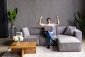 Great thing. Euphoric young man sit on couch by laptop screen shout super raise fists in winner gesture get good news job offer Royalty Free Stock Photo