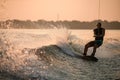 Great view of splashing wave and muscular man energetically riding wakeboard.