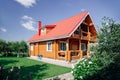 Great wooden cottage house with red tile roof, lawn area on left and cherry trees orchard behind house and front flower Royalty Free Stock Photo