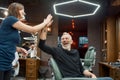 Great work. Happy middle-aged man giving five to young and cute barber girl while sitting in armchair in the barbershop